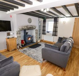 A living room with a fireplace wood stove two gray sofas a wall-mounted TV and a wooden door at Min-y-rhos in Edern