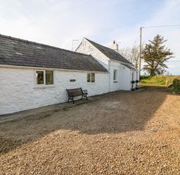A white stone cottage with a slate roof a bench outside and a gravel driveway at Min-y-rhos in Edern
