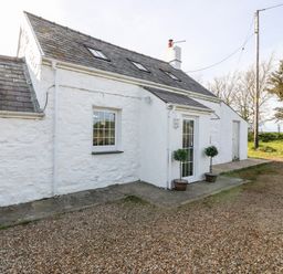 The exterior of a white stone cottage with a gravel driveway and two potted plants near a glass door at Min-y-rhos in Edern