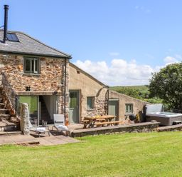 An outdoor patio with lounge chairs a picnic table a barbecue hot tub and grassy lawn at Sunbury Barn in St Agnes