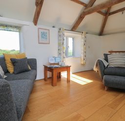 A living room with gray sofa and armchair wooden table and exposed wooden beams at Sunbury Barn in St Agnes