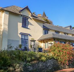 A building with beige walls and blue window frames surrounded by plants and flowers at C S Lewis Balcony in Lynton
