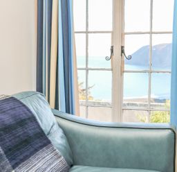 A blue leather sofa near windows with blue and cream curtains overlooking the sea at C S Lewis Balcony in Lynton