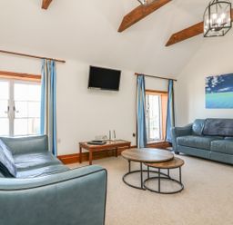 A living room with two blue sofas a round wooden coffee table two windows with blue curtains a wall mounted TV and a painting at C S Lewis Balcony in Lynton