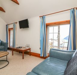 A sitting room with blue sofas a wall-mounted tv blue and white curtains and a wooden coffee table at C S Lewis Balcony in Lynton