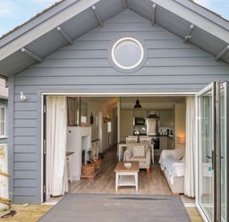 A small cabin with folding glass doors open to a living area with chairs a table and a kitchen at Sea Breeze in The Bay near Filey