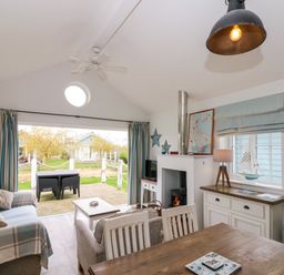 An open plan living and dining area with sofas a dining table a coffee table a wood burning stove and a deck with outdoor furniture at Sea Breeze The Bay near Filey