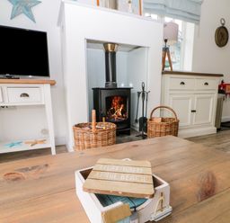 A living room with a wood-burning stove two wicker baskets a wooden table with a decorative box and a TV on a white stand at Sea Breeze The Bay near Filey