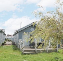A pair of blue wooden cottages with chimneys a small deck with chairs and a tree in the grass between cottages at Sea Breeze The Bay near Filey