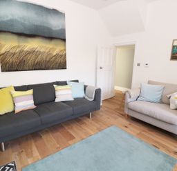 A living room with a dark gray sofa and light gray armchair with pillows a blue rug on the floor and artwork on the walls at Teviot Cottage in Corbridge