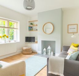 A living room with a gray sofa with pillows a beige armchair a blue rug a small television and sunflowers on a windowsill at Teviot Cottage in Corbridge