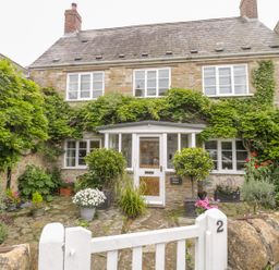 A stone house with climbing plants around windows and door with potted plants in front and a white gate at Market House in Abbotsbury