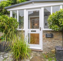 A white door with glass panels surrounded by stone walls and plants at Market House in Abbotsbury
