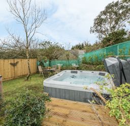 A garden with a hot tub on a wooden deck and a table with chairs near a wooden fence at Crift Farm Cottage in Lanlivery near Lostwithiel