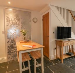 A dining area with a wooden table and benches a small wooden TV stand with a TV and stairs in the background at Crift Farm Cottage Lanlivery near Lostwithiel