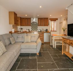 An open living room and kitchen with a sectional sofa kitchen cabinets dining table and television at Crift Farm Cottage Lanlivery near Lostwithiel