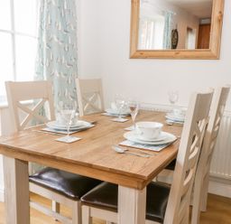 A dining table set with plates glasses and cutlery with chairs around at Bayside Cottage The Bay near Filey