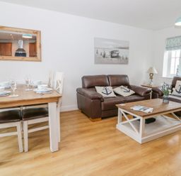 A living room with a dining table set with dishes a brown leather sofas and a wooden coffee table at Bayside Cottage in The Bay near Filey
