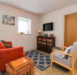 A small sitting room with an orange sofa a gray armchair a wooden cabinet with wicker baskets and a wall-mounted television at Wallerthwaite Barn Cottage in Markington