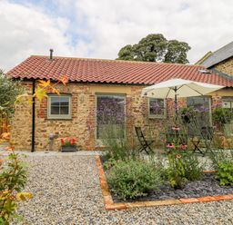 A stone cottage with tiled roof a gravel path and a flower bed with an umbrella at Wallerthwaite Barn Cottage in Markington