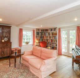 A living room with a pink sofa armchairs a wooden cabinet bookshelf a piano and French doors at Church View in Salisbury