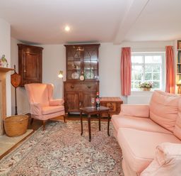 A living room with pink upholstered sofa and armchair a wooden cabinet a small wooden table with wine on a rug near a window with pink curtains at Church View in Salisbury