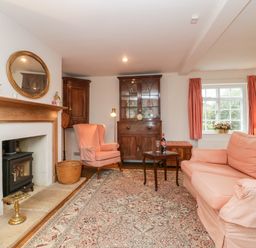 A sitting room with a fireplace a pink armchair a wooden cabinet and a pink sofa at Church View in Salisbury