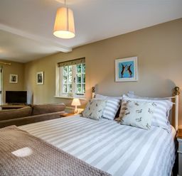 A bedroom with a striped bed and two cushions facing a sofa and TV at Cider Press in Burford
