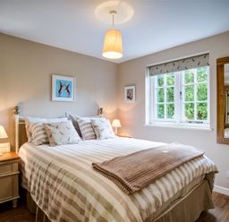 A bedroom with a striped bedspread bedside tables lamps and windows at Cider Press in Burford