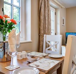 A dining table set for two with plates glasses and cutlery near a window with flowers in a vase and a champagne bottle in an ice bucket at Cider Press in Burford