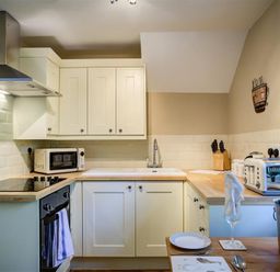 A kitchen with white cabinets a microwave a toaster a knife block and a table set with a plate and glass at Cider Press in Burford