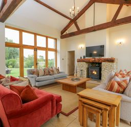 A living room with two sofas a coffee table a fireplace and a large window at Lower Farm Barn in Aston Near Bampton