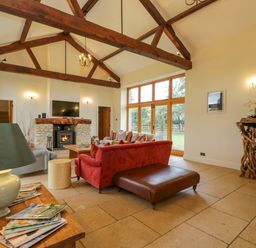 A living room with exposed wooden beams a fireplace and large windows at Lower Farm Barn Aston Near Bampton