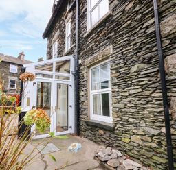 Stone exterior wall of a house with a white framed glass door and window with dried flowers in the foreground at Giddy Goose in Windermere