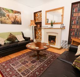 A living room with two leather sofas a round wooden coffee table a fireplace stacked wood and a bookshelf wallpaper at Giddy Goose in Windermere