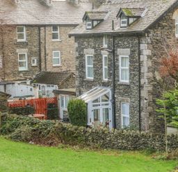 Stone houses with slate roofs behind a stone wall and green lawn at Giddy Goose in Windermere