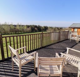A wooden deck with chairs overlooking a grassy area and trees at Percy Wood Country Park in Swarland