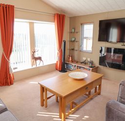 A living room with a wooden coffee table sofa orange curtains a mounted television and a fireplace at Percy Wood Country Park in Swarland