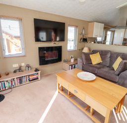 A living room with a gray couch yellow pillows wooden coffee table mounted TV and fireplace at Percy Wood Country Park Swarland