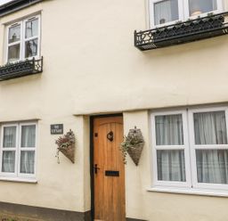 A cottage exterior with a wooden door two windows with flower boxes and wall planters at Beach Retreat in Instow