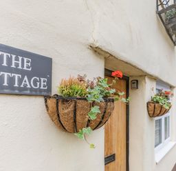 The exterior of a cottage with flower baskets and a sign that reads The Cottage at Beach Retreat in Instow