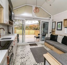 A kitchen and living area with patterned floor tiles a gray sofa and sliding glass doors leading to a wooden deck at Meadow Retreat in Nantmel near Rhayader