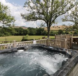 An outdoor area with a hot tub and a wooden table at Meadow Retreat Nantmel near Rhayader