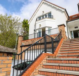 Stairs leading up to a white building with red roof and black railings at Seashells in Tenby