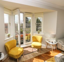 A living room corner with two yellow chairs a small white table with a lamp and a gray sofa at Seashells in Tenby