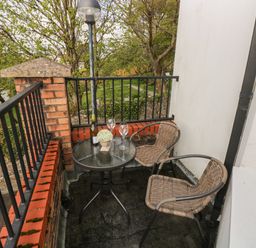 A small balcony with two wicker chairs a round glass table holding a wine bottle two glasses and a small plant at Seashells in Tenby