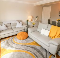 A living room with two gray sofas a yellow throw and knitted cushion a patterned rug and a glass dining table at Seashells in Tenby