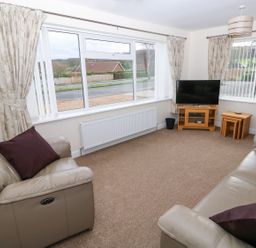 A living room with two leather sofas a television on a wooden stand and beige curtains at Elliotts Retreat in Sheringham