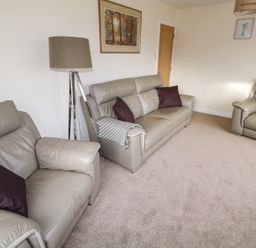 A living room with grey leather sofas a floor lamp and framed pictures on the wall at Elliotts Retreat in Sheringham