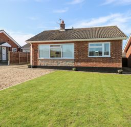 A brick detached house with a lawn and gravel driveway at Elliotts Retreat in Sheringham